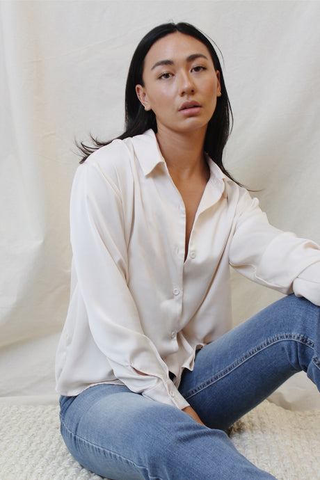 With a silky sheen to this creme colored classic, introduce this staple to your closet. Featuring button-down detailing, button cuffed sleeves and timeless collar, the look is elevated with its boyfriend fit.